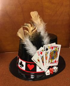 a black hat with playing cards, dice and feathers on it sitting on a table