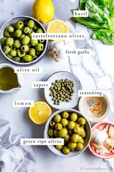 the ingredients for an olive salad laid out on a marble counter top with lemons, garlic, and basil