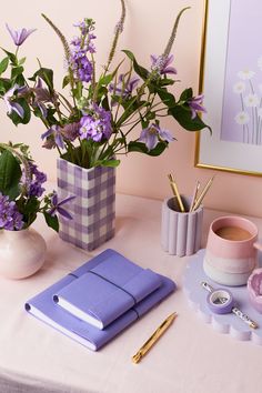 purple flowers are in vases on a table next to a notepad and pen