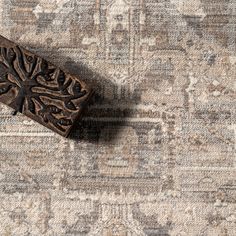 a piece of wood sitting on top of a gray and beige rug with an intricate design