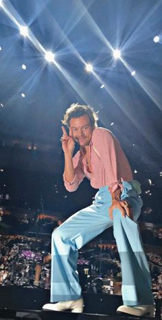 a man standing on top of a stage holding a cell phone to his ear and wearing blue pants