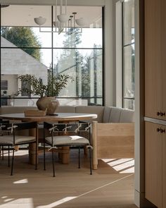 a dining room table with chairs and a bench in front of large windows that look out onto the backyard