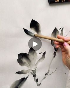 a person is holding a paintbrush and painting flowers on a white paper with black ink