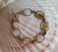 This unique mother of pearl bracelet has coin beads enclosed in silver pewter oval shaped links  (20 mm) separated by pewter spacers. The closure is a pretty silver toggle and clasp. Two lengths available, 7 inches and 8 inches. Convo La Marquise with your choice. Comes in a red storage pouch. See the matching necklace and earrings. Silver Circular Beaded Jewelry, Silver Beaded Circular Jewelry, Silver Beaded Mother Of Pearl Jewelry, Vintage Silver Round Beaded Bracelets, Vintage Silver Beaded Bracelet, Vintage Silver Beaded Bracelets, Silver Mother Of Pearl Round Bead Jewelry, Vintage Silver Beaded Round Bracelets, Silver Oval Beaded Jewelry