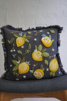 a black pillow with yellow lemons on it sitting on a chair next to a white wall