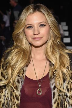 a woman with long blonde hair wearing a leopard print jacket and red tank top is smiling at the camera