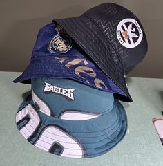 Have an old sports jersey that you just can't get rid of? Turn it into a bucket hat!  You send us your soccer, football, baseball or hockey jersey (or any other sport!) and we'll custom make you a one-of-a-kind bucket hat.  Each hat is made with a hand-drafted pattern with a modern, streetwear style fit.  The jersey material will be reinforced for structure and durability.   Three sizes available: Big Kid (fits my 10 year old, approx. 21in/53.5cm), Standard (up to 23.5in/59cm), Large (25in/63cm) Sporty Bucket Hat For Sports, Sporty Black Bucket Hat For Sports, Blue Sports Bucket Hat, Blue Bucket Hat For Sports, Casual Team-colored Hats With Letter Print, Hip Hop Hat With Letter Print For Sports Events, Streetwear Bucket Hat With Letter Print, Sporty Hats With Letter Print For Sports Season, Customizable Casual Sports Hats