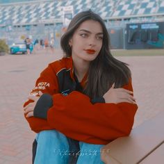 a woman sitting on a bench with her arms crossed and looking at the camera while wearing an orange sweatshirt