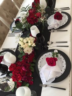 the table is set with black and white plates, silverware, and red flowers