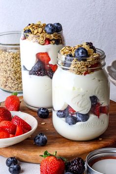 two jars filled with yogurt, granola and berries on a cutting board