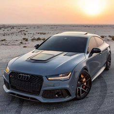 the front end of a grey car parked in an open field with sunset behind it