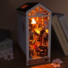 an open doll house sitting on top of a wooden table next to books and flowers