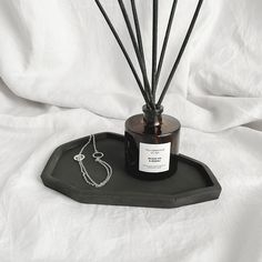 a black tray with a candle and some sticks in it on a white cloth background