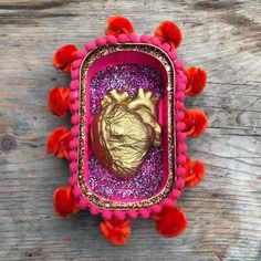 a heart shaped brooch with red and pink pom poms around it on a wooden surface