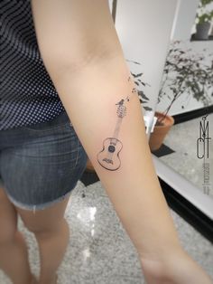 a woman's arm with a guitar tattoo on the left side of her arm