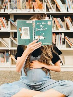 a woman sitting on the floor holding up a book in front of her face, reading are you my mother?