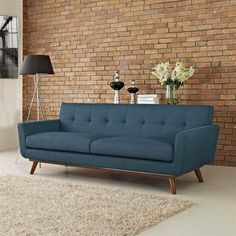 a blue couch sitting in front of a brick wall next to a lamp and rug