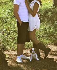 a man and woman standing next to each other in the woods with a small dog