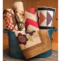 a bucket filled with lots of quilts on top of a wooden floor