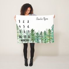 a woman is holding up a large calendar sign with trees on it and the date