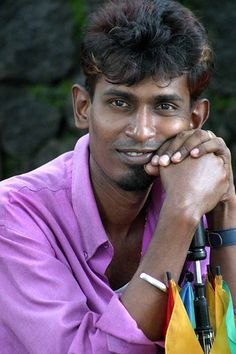 a man sitting down with an umbrella in his hand and looking at the camera while wearing a purple shirt