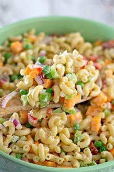 a green bowl filled with macaroni salad and a wooden spoon in the bowl