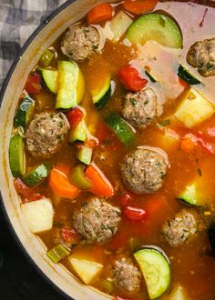 a pot filled with meatballs and vegetables on top of a table next to a towel