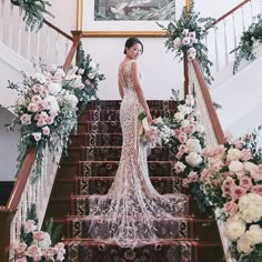 a woman in a wedding dress standing on the stairs with flowers and greenery behind her