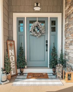 a blue front door with two christmas trees on the side and a welcome mat in front