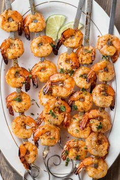 shrimp skewers on a white plate with lime wedges