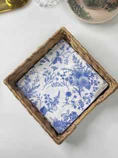 a blue and white floral print napkin in a wooden frame on a table with other dishes