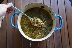 a person holding a spoon in a pot full of soup on a wooden table top