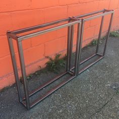 two metal frames sitting next to each other on the ground near a red brick wall