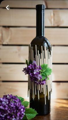 a wine bottle with sticks sticking out of it and flowers in front of the bottle