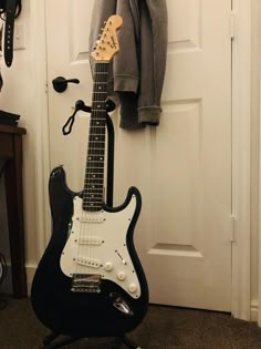 an electric guitar sitting on top of a stand next to a coat rack and door