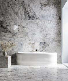 a white bath tub sitting next to a wall with marble on the walls and floor