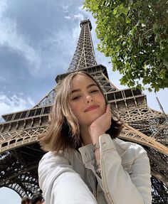 a woman standing in front of the eiffel tower with her hand on her chin