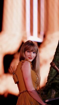 a woman in an orange dress standing next to a tree with her hand on the piano