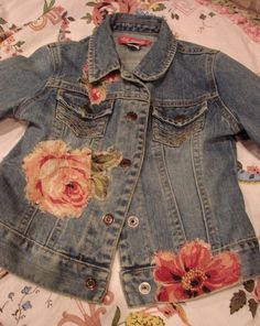 an old jean jacket with flowers on the front and back, sitting on top of a bed