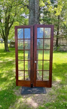 an open wooden door sitting next to a tree in the grass on top of a field