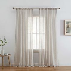 a living room with white curtains and a wooden table in front of the window,