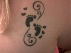 a woman's back with a tattoo design on her left shoulder and foot prints in the shape of hearts