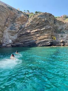 two people swimming in the ocean near some cliffs