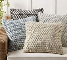 four pillows sitting on top of a white couch next to a potted plant and wicker basket