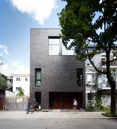 two people are walking in front of a black brick building with garage doors and windows