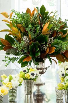 a table topped with vases filled with flowers and greenery