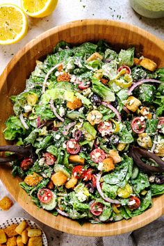 a wooden bowl filled with salad next to sliced lemons and other food on a table