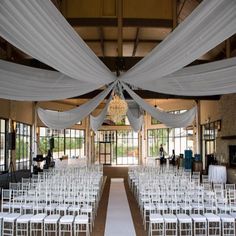 an indoor wedding venue with white chairs and draping