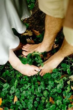 two people standing on top of green leaves in the grass with their bare feet touching each other