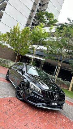 a black mercedes cla parked in front of a tall building with trees and bushes